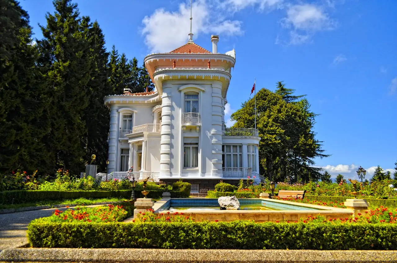 Conciergerie à Saint-Jean-Cap-Ferrat : Valorisez votre propriété d’exception A beautiful white mansion surrounded by lush gardens and a fountain on a sunny day.